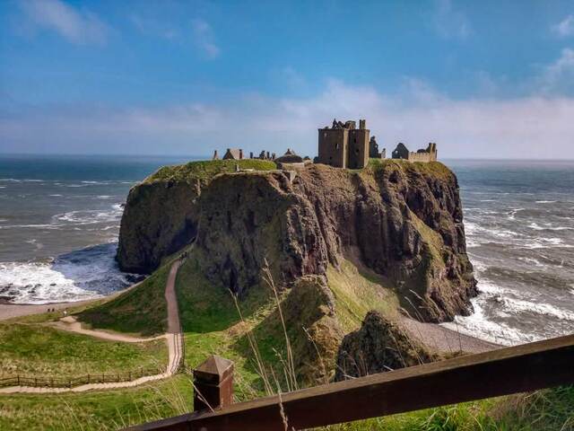 The winding path leading to the castle offers stunning views of the surrounding cliffs, rocky shores, and rolling waves of the North Sea