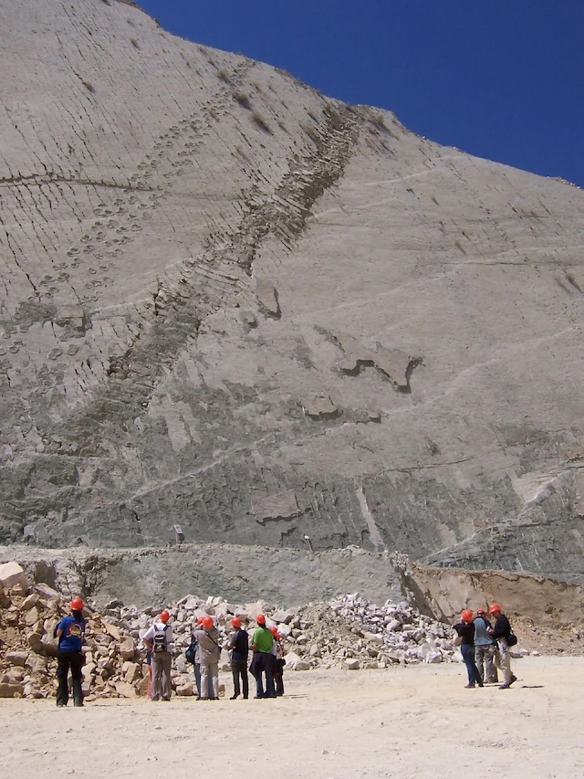 Visitors stand in awe beneath the towering limestone wall of Cal Orcko, Bolivia, showcasing an incredible array of preserved dinosaur footprints