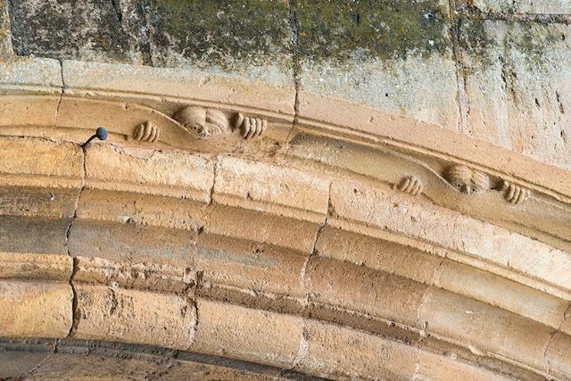 "The Peeker" as seen along the archway of the Abbey of Sainte Foy, its hands and eyes emerging from the stone with a mischievous expression