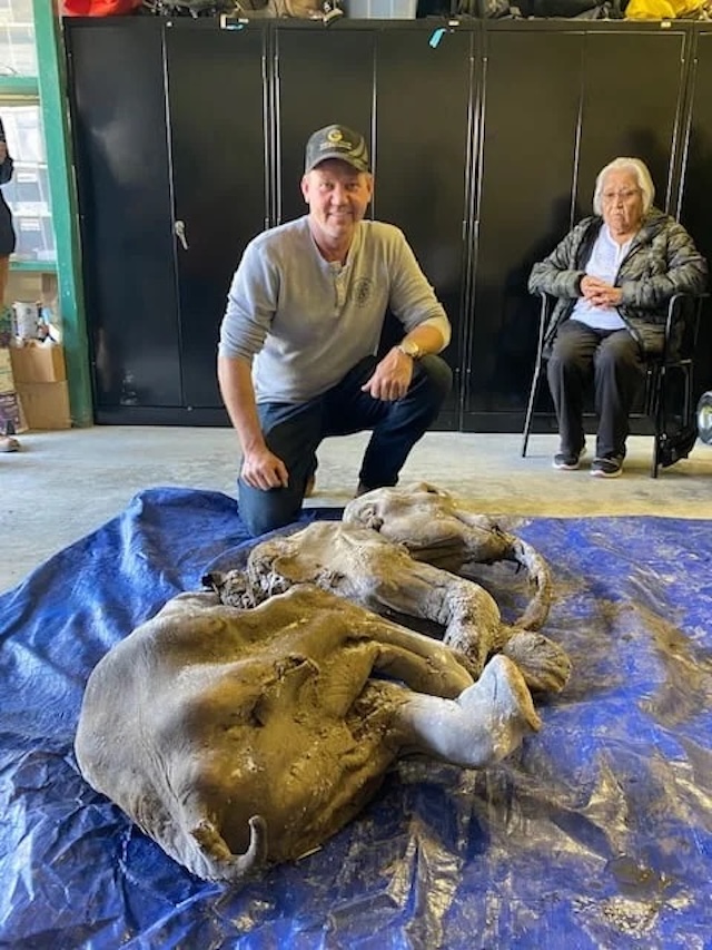 A researcher poses with the mummified baby woolly mammoth, showcasing the creature's well-preserved condition after 30,000 years in the permafrost