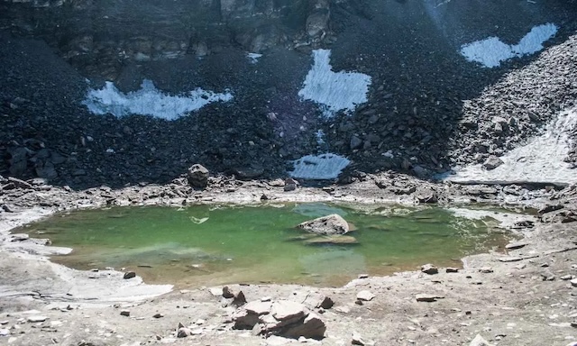 The tranquil, emerald waters of Roopkund Lake, concealing hundreds of human remains, contrast with the stark, rocky Himalayan terrain