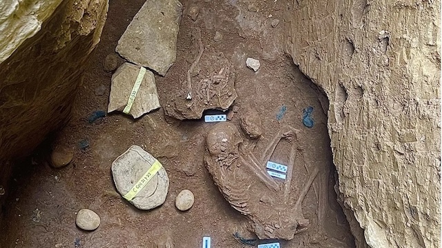 A closer view of the burial site within one of the caves, revealing skeletal remains and scattered artifacts buried alongside the deceased