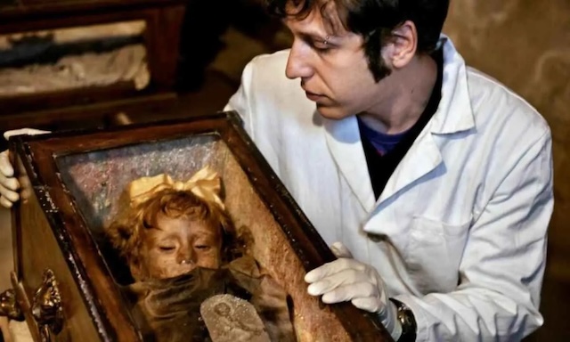 A forensic scientist carefully examines the body of Rosalia Lombardo, showcasing the remarkable preservation of her mummified remains, including her seemingly lifelike appearanc