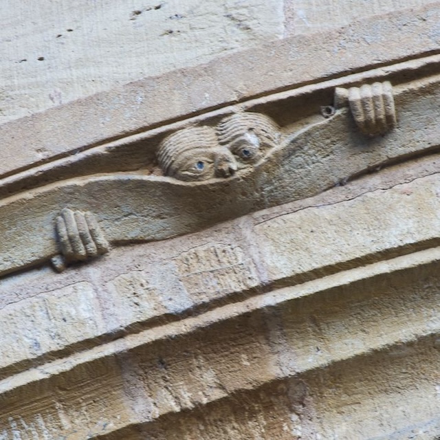 A detailed view of "The Peeker," showcasing its expressive face and hands carved into the stone, a reminder of the whimsical humor present in medieval architecture.