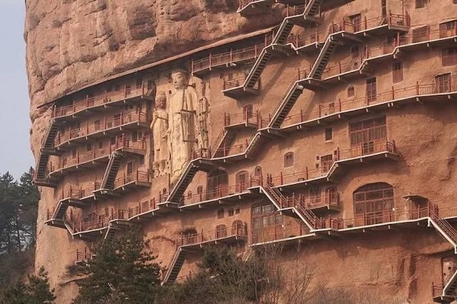 A complex of cave homes and statues carved into a steep cliff, exemplifying the ingenuity of ancient Chinese construction