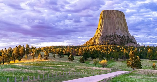 Devils Tower is bathed in golden light as the sun sets, adding to the monument’s mystical and awe-inspiring atmosphere