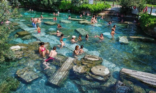 Cleopatra's Pool bustling with visitors, who immerse themselves in the rich history and therapeutic waters of this ancient spa, surrounded by remnants of Roman architecture