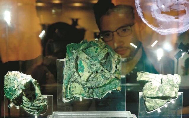 The Antikythera Mechanism on display, with a visitor examining the ancient gears that puzzled historians for years