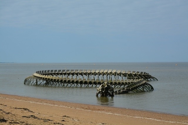 As the tide goes out, the full extent of the "Serpent d'Océan" emerges from the sand, resembling an ancient sea creature resting along the beach