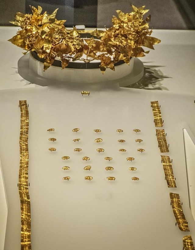 Exquisite display of a gold wreath and other ancient burial artifacts in a museum exhibit, highlighting ancient Greek craftsmanship and funerary traditions