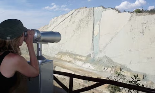 A visitor peers through a telescope, marveling at the intricate network of ancient dinosaur tracks etched into the cliffside