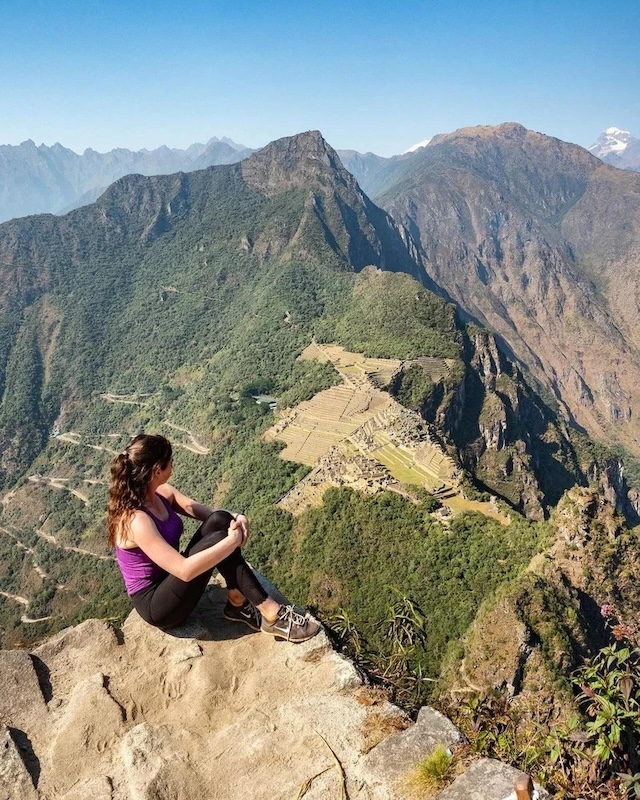 A hiker admires the breathtaking panoramic view of the Machu Picchu citadel and surrounding valleys from the summit of Huayna Picchu