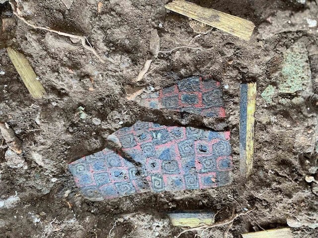 A colorful tile fragment emerges from the earth, a small piece of an ancient puzzle