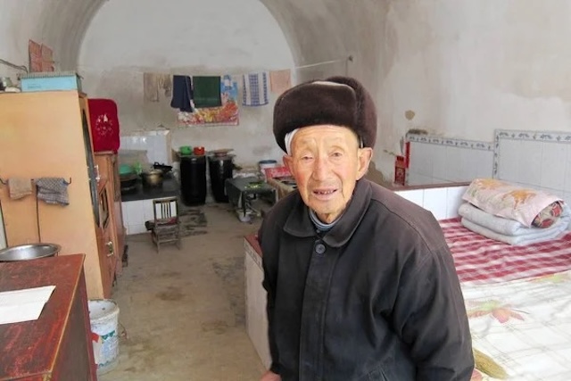 An elderly resident in the interior of a modernized cave dwelling, showing how traditional homes have been adapted for comfortable living