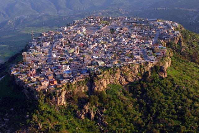 An aerial view of the entire city of Amadiyah, showcasing its strategic position atop a small plateau surrounded by steep cliffs