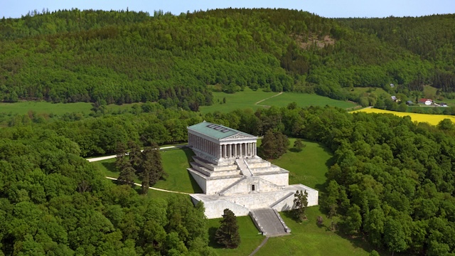 A stunning side view of Walhalla, surrounded by lush greenery and rolling hills, emphasizing the monument's integration with its natural surroundings