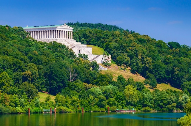 Walhalla as seen from the banks of the Danube River, framed by vibrant foliage, showcasing its grandeur and serene beauty in perfect harmony with the landscape