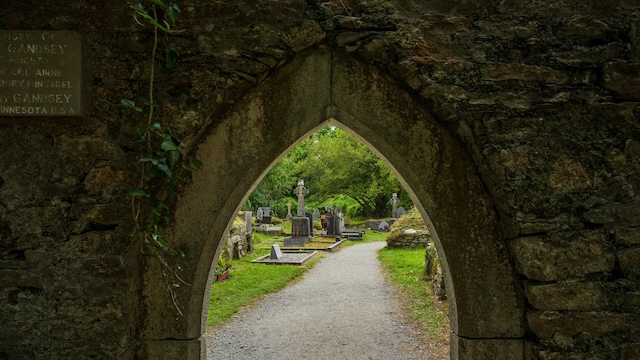 A picturesque archway at Muckross Abbey, offering a glimpse into the surrounding graveyard and the natural beauty of the park