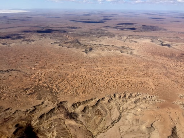 Aerial view of the vast and rugged Australian outback, with the faint outline of the mysterious Marree Man etched into the desert landscape.