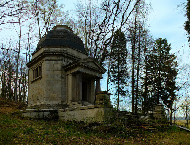 The front view of the decaying mausoleum, overgrown with wild vegetation, showcasing its haunting, gothic architecture.