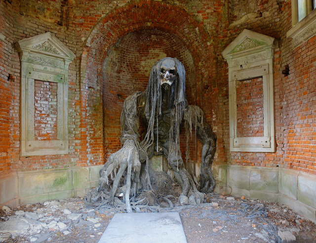 The demon statue in full view, framed by ornate yet decaying architectural elements, a forgotten piece of history.