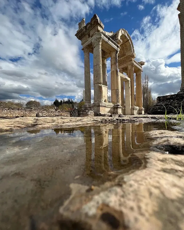 A beautifully preserved Roman gateway reflecting on a puddle, symbolizing the enduring legacy of Sagalassos.