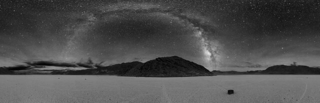 A breathtaking panorama of the Milky Way illuminates the desert, with the winding tracks of the sailing stones visible below—spot the stone on the right.