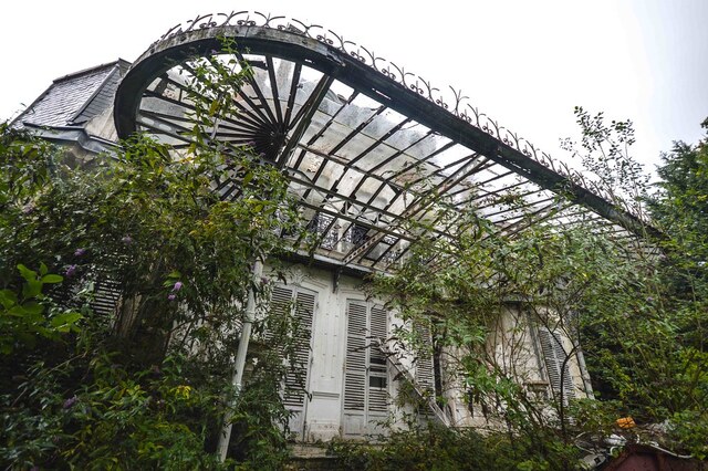 A close-up of the intricate wrought-iron canopy that frames the entryway, now overgrown with greenery.