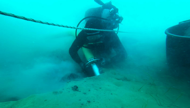 A diver meticulously clears sediment from the shipwreck using specialized equipment, ensuring the integrity of the artifacts. 