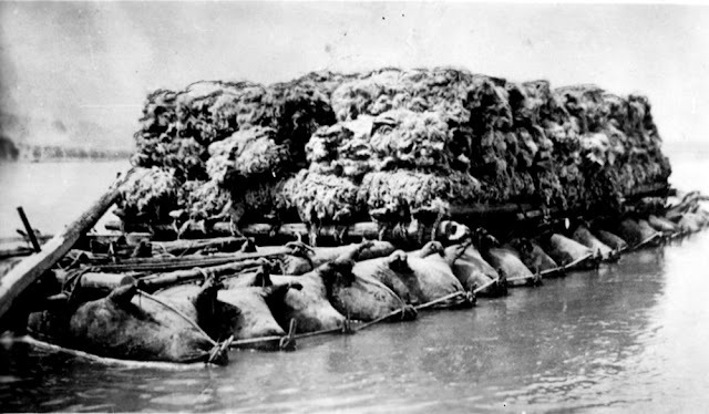 A fully loaded raft of inflated bullock skins transporting goods across a river, showcasing the method's versatility.