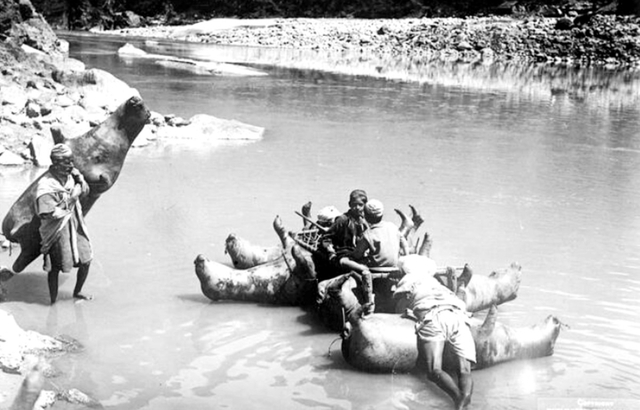 A group of men demonstrating the use of inflated bullock skins to ferry passengers across a river.