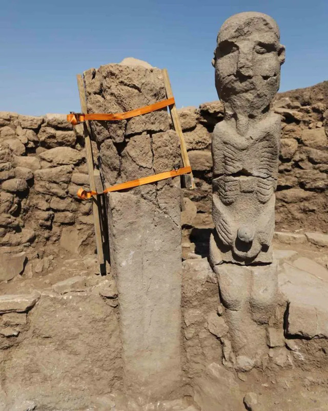 A partially restored stone statue with visible repairs, representing a standing figure alongside a reconstructed column.