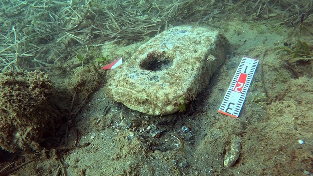 A prehistoric stone anchor with a central hole, believed to have been fitted with wooden flukes, showcasing ancient seafaring techniques.