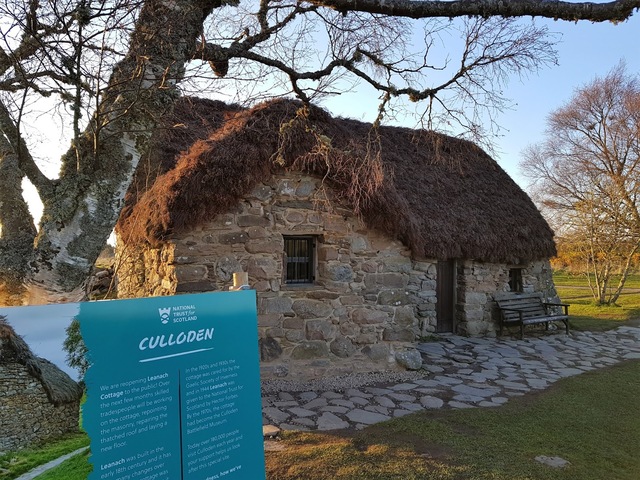 A view of Old Leanach Cottage, accompanied by a sign explaining its connection to the Battle of Culloden.