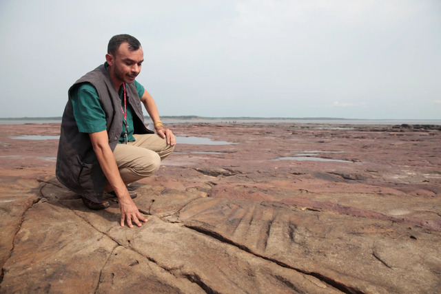 Archaeologist Jaime de Santana surveys ancient tool-sharpening marks on Amazon river rocks, revealed by the falling water level during the drought in Manaus.