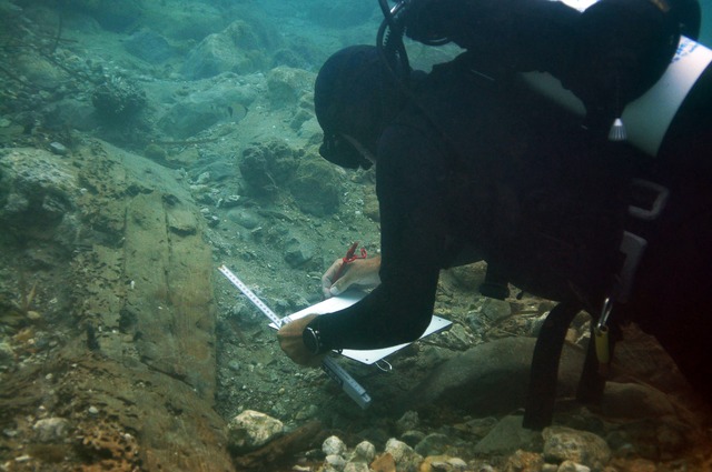 Archaeologists meticulously document the wooden hull of the 2,500-year-old shipwreck using precise underwater measuring tools.