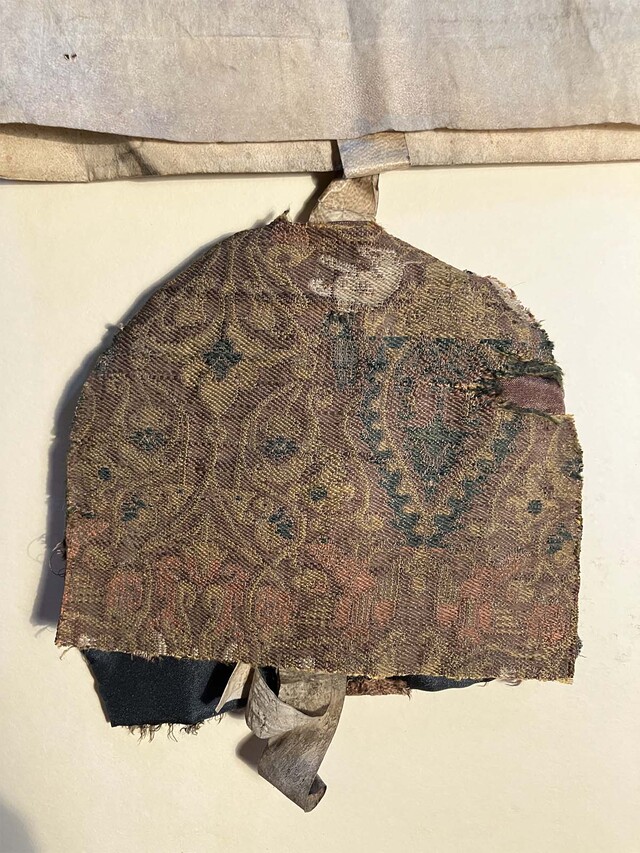 The silk bag sewn to protect King Henry III's wax seal impression, featuring intricate patterns of hares and floral motifs, matches Charlemagne’s burial shroud.