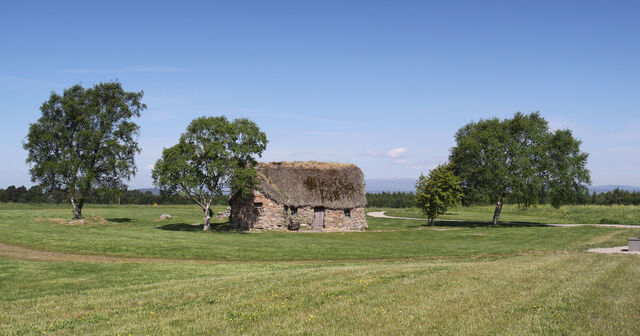 Old Leanach Cottage sitting alone in a vast green field, surrounded by serenity and history.