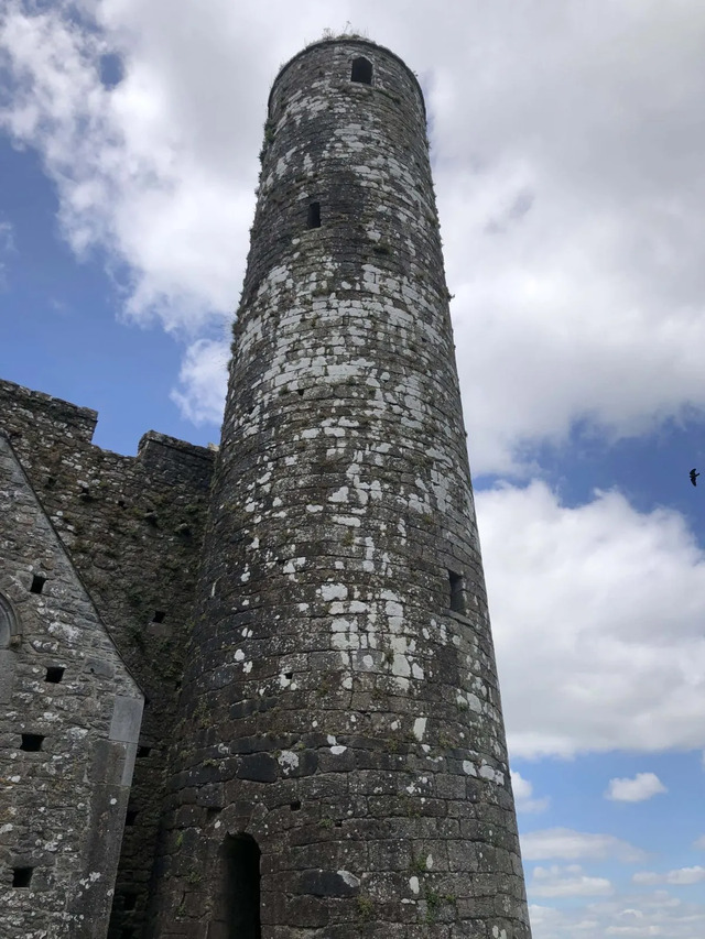 The Rock of Cashel's towering silhouette dominates the horizon, a beacon of Ireland's medieval history against a vibrant blue sky.