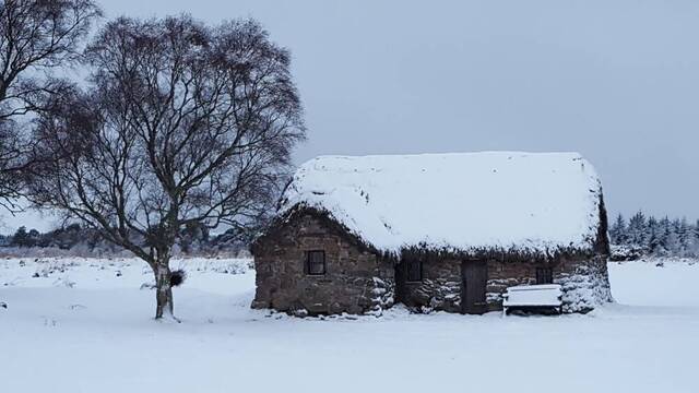 The cottage is covered in a blanket of snow, showcasing its resilience against time and nature.