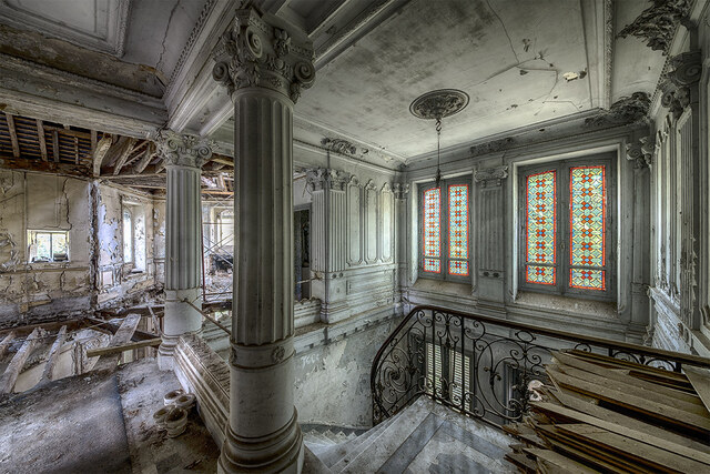 The majestic interior stairway adorned with columns and stained glass, radiating faded opulence.