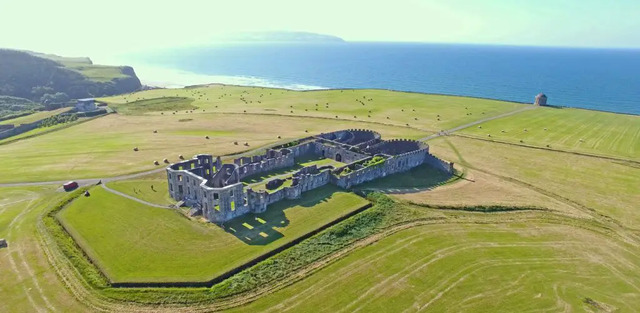 The vast green fields surround the majestic ruins of Downhill House, with the Atlantic Ocean in the background.