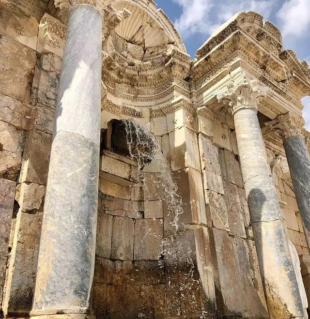 Water flowing from the Nymphaeum’s fountain, surrounded by towering columns and ornate details.