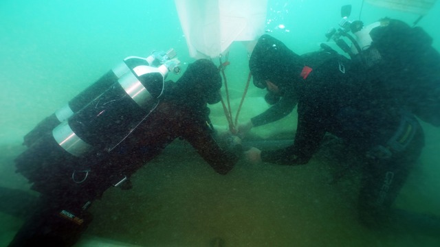 Researchers work in tandem to lift delicate timbers and ingots from the ocean floor, ensuring minimal damage during recovery. 