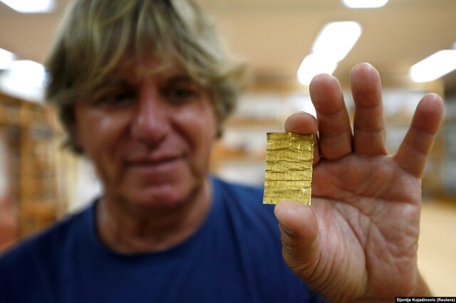 A 2016 photograph shows Korac holding a golden amulet unearthed in the ancient city, a dazzling artifact of Roman craftsmanship.