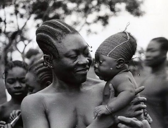 A Mangbetu mother lovingly holding her baby, whose head is wrapped to create the elongated shape associated with status and beauty in their culture.