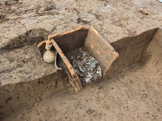 A brick-slab grave holds cremated human remains alongside a handled jug, with a rib bone—likely from a food offering—found carefully placed near the deceased. (Credit: LAD, Roth)