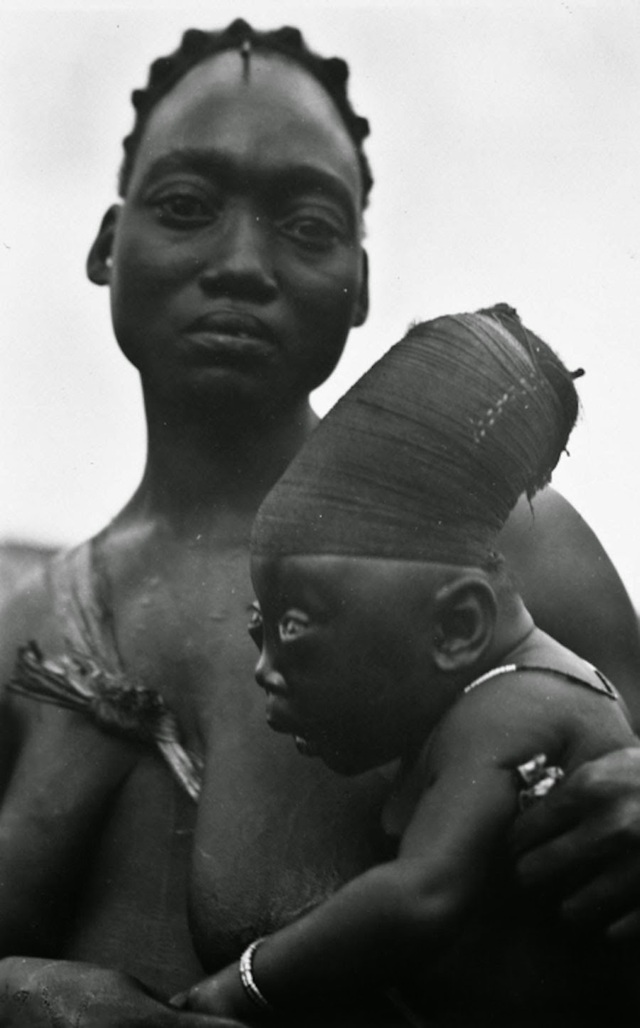 A close-up of a Mangbetu woman and her baby, highlighting the cranial deformation process that begins in infancy. The wrapped cloth used for Lipombo can be seen on the baby’s head.