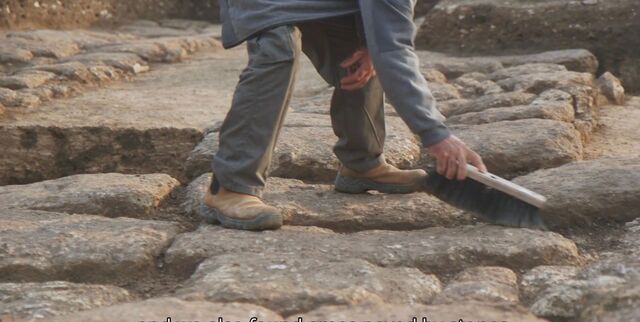 A close-up of an archaeologist carefully brushing away soil from the ancient Roman stone pavement to preserve its intricate details.