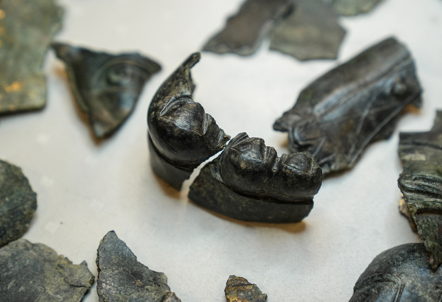 A close-up of two intricately carved bronze facial fragments from statues, emphasizing the skill of ancient sculptors.